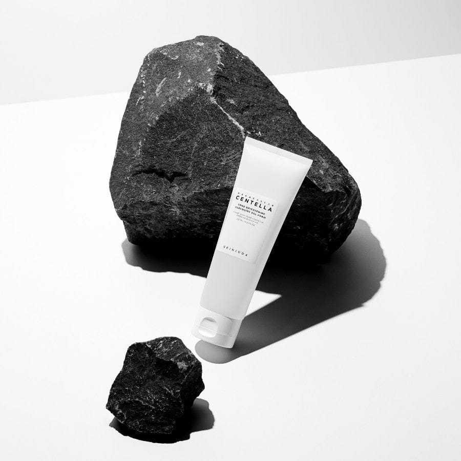 Espuma limpiadora SKIN1004 Tone Brightening Cleansing Gel Foam 125ml sobre fondo blanco con rocas oscuras.